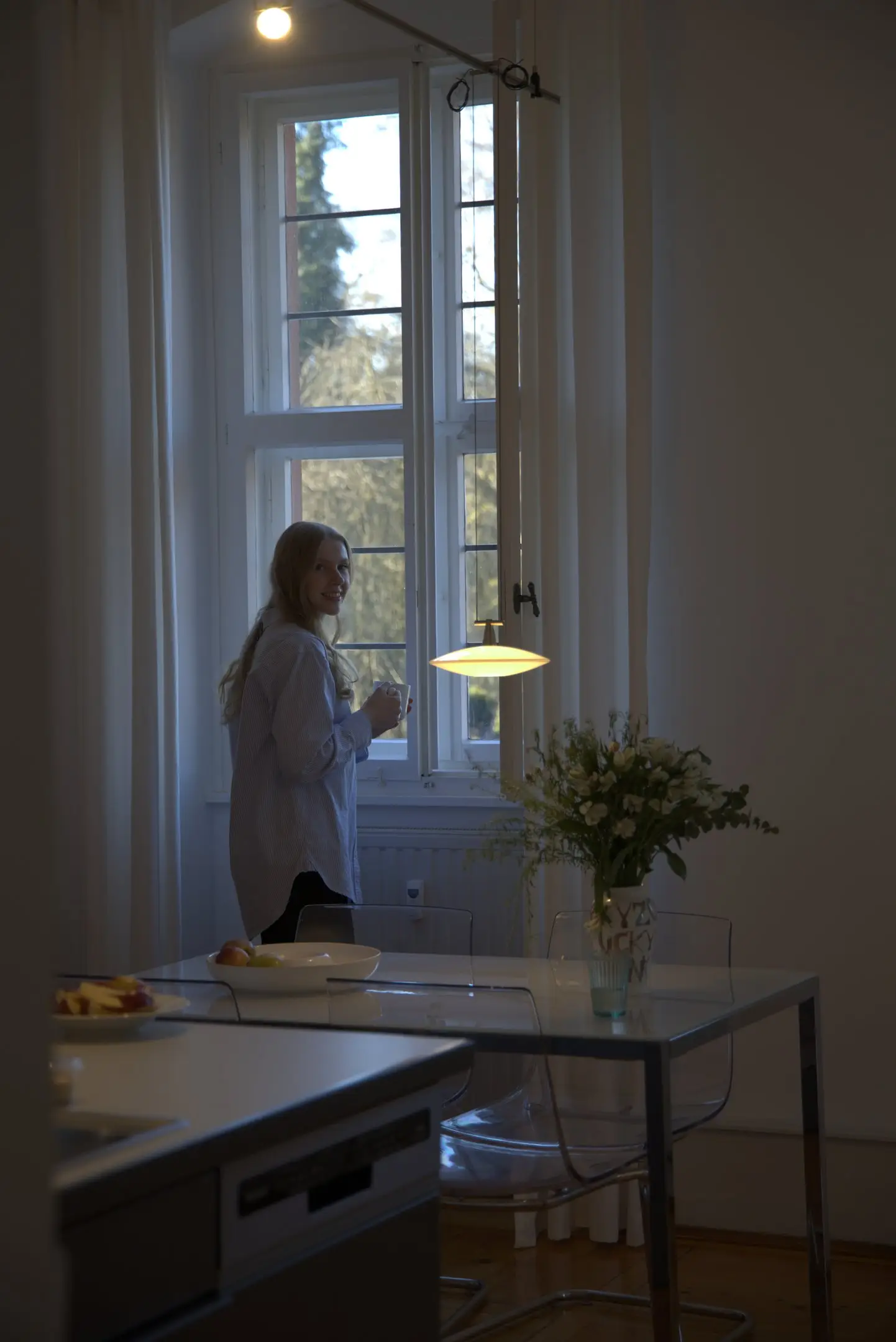 Frau am Fenster einer hellen Küche mit Blumenstrauß