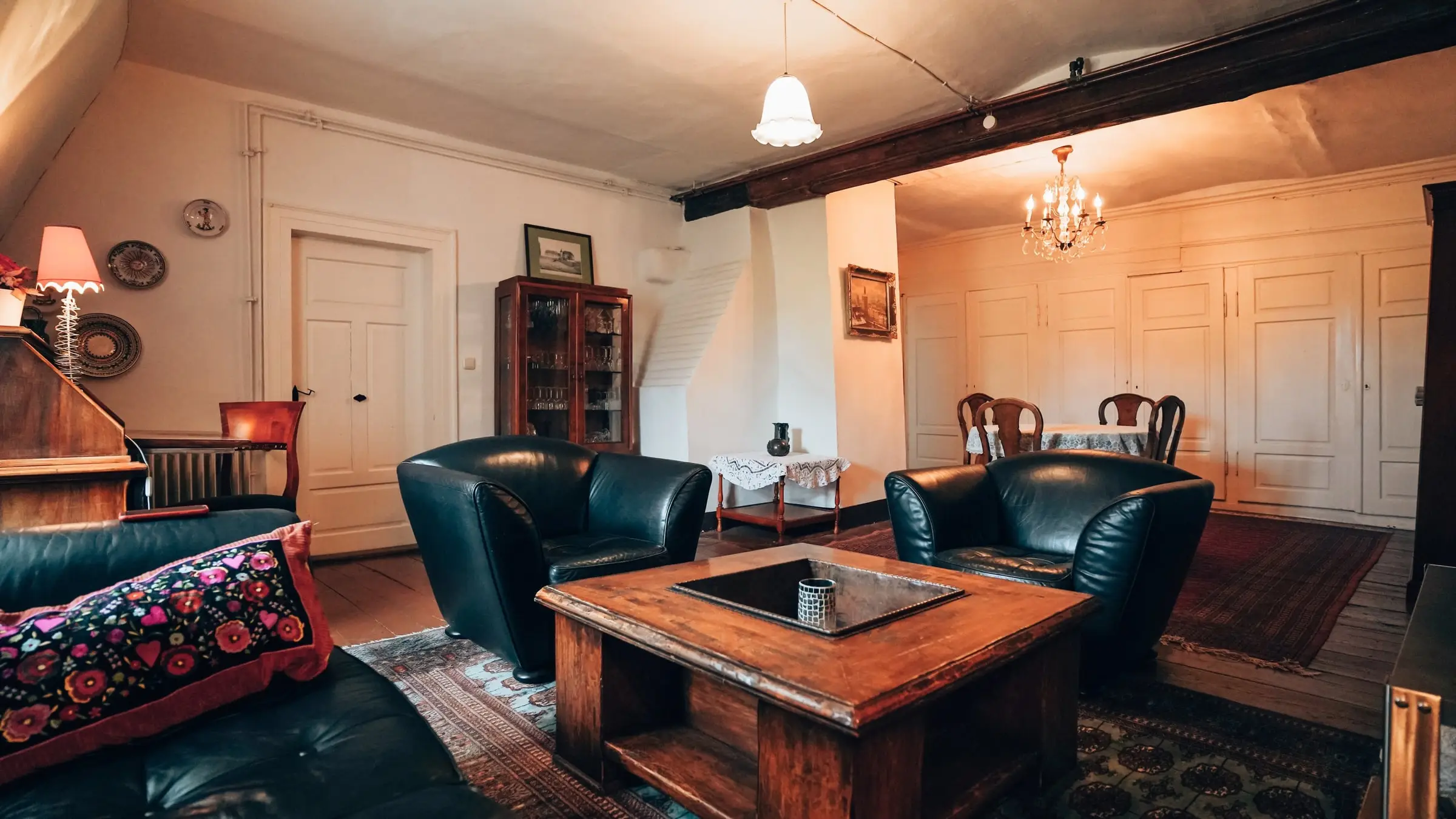 Wohnzimmer mit grünen Ledersesseln, Couchtisch und Essplatz unter Holzbalken